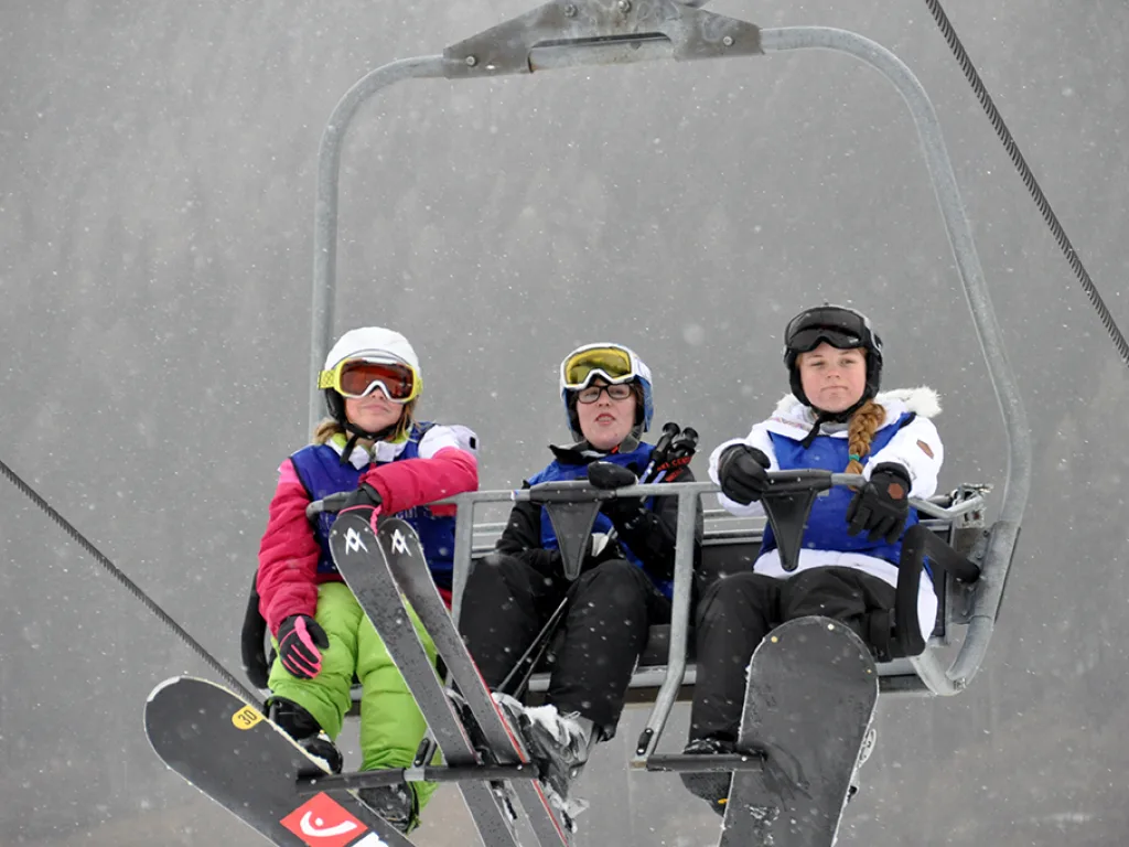 Drei Jugendliche mit Snowboards im Sessellift.